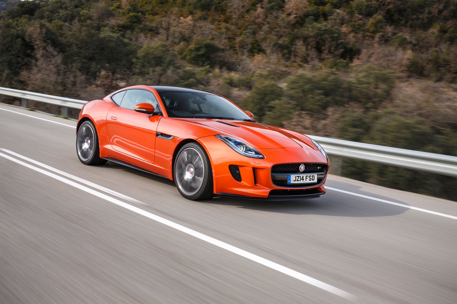 An orange Jaguar F-Type sports car speeds along a scenic road, showcasing its sleek design and vibrant color in this stunning 4K Ultra HD desktop wallpaper.