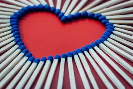 Close-up photography of blue-tipped matches arranged into a heart on a red background — 5K Ultra HD PC desktop wallpaper/background.