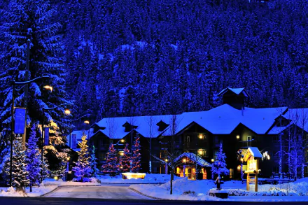 A serene night scene in Canada featuring a beautifully lit hotel surrounded by a snow-covered landscape and decorated Christmas trees, creating a festive winter atmosphere.