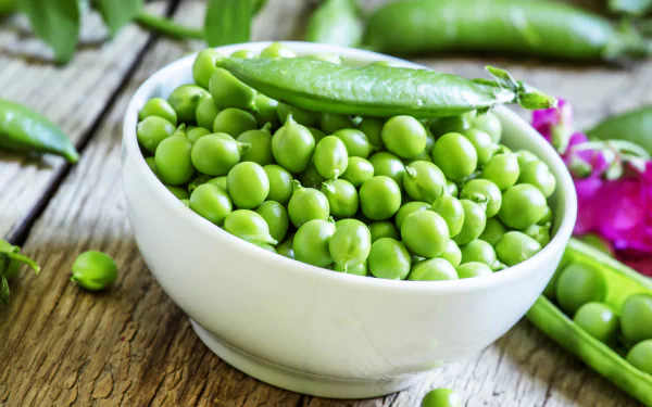A vibrant 4K Ultra HD desktop wallpaper featuring fresh green peas in a white bowl and pea pods on a rustic wooden surface.
