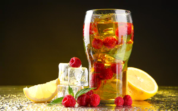 A refreshing glass drink filled with ice cubes, raspberries, and lemon, beautifully displayed against a dark background, enhancing its vibrant colors in this 4K Ultra HD wallpaper.