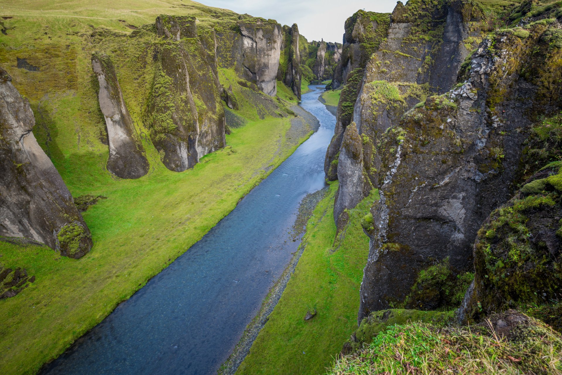 HD desktop wallpaper of a deep river canyon in Iceland, surrounded by tall cliffs covered in green moss and grass, showcasing stunning natural landscape.