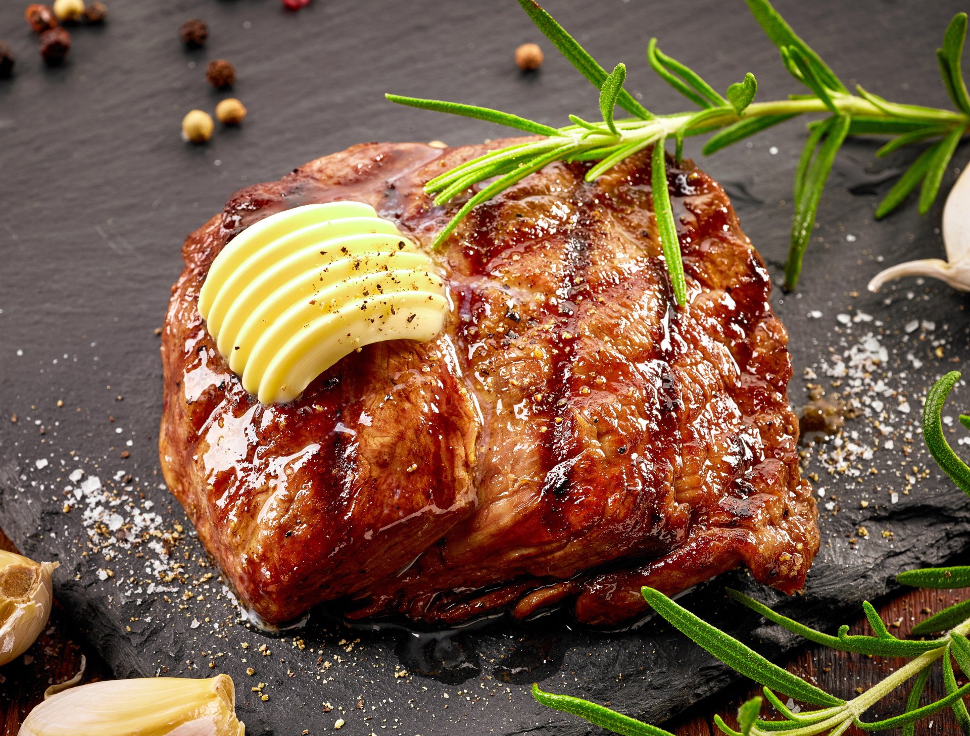 5K Ultra HD PC desktop wallpaper: close-up of a grilled steak — butter-topped meat glistening with grill marks, rosemary sprigs, coarse salt and pepper, appetizing food background.