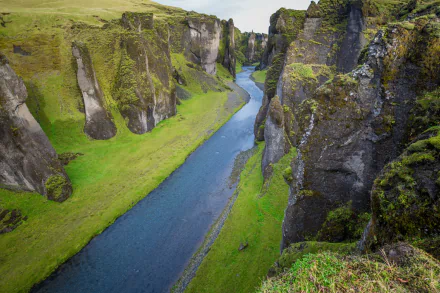 HD desktop wallpaper of a deep river canyon in Iceland, surrounded by tall cliffs covered in green moss and grass, showcasing stunning natural landscape.