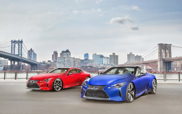 HD desktop wallpaper featuring two Lexus LC 500 grand tourer cars, one red and one blue, parked with a city skyline and bridges in the background.