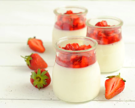 2K Quad HD PC desktop wallpaper/background showing glass jars of creamy yogurt topped with diced strawberries, surrounded by whole and halved strawberries — fruit, strawberry, glass food scene.