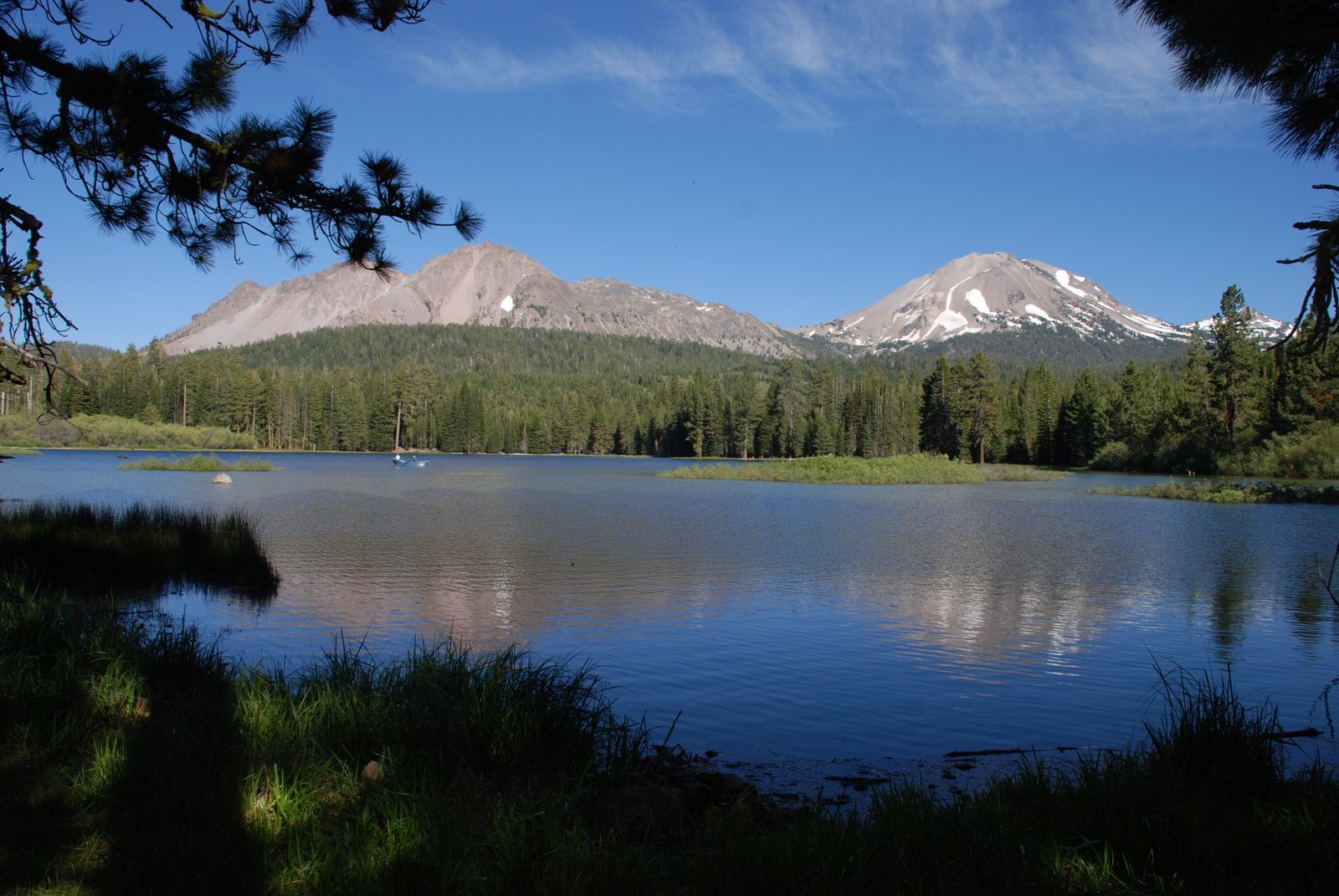 HD desktop wallpaper featuring a serene nature landscape with a calm lake, lush green forest, and two snow-capped mountains under a clear blue sky.