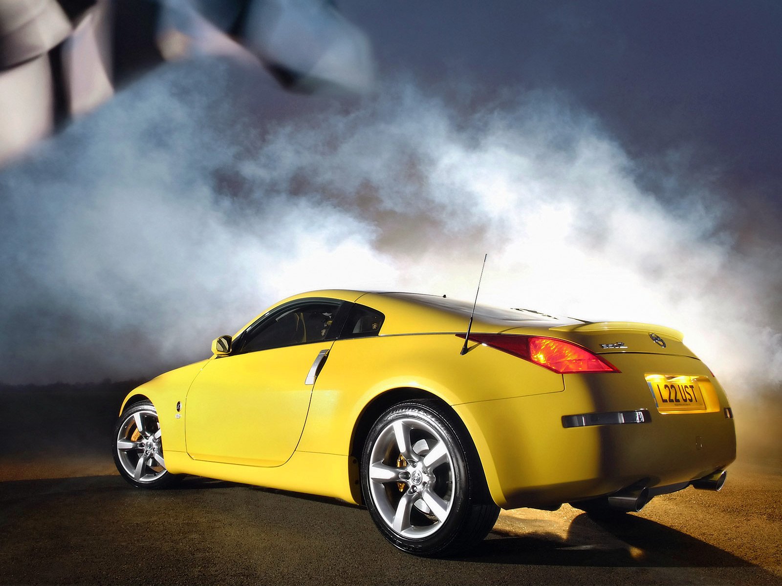 Yellow Nissan 350Z vehicle in rear three-quarter view amid smoke and dramatic lighting — HD PC desktop wallpaper/background.