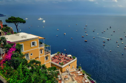 A vibrant coastal scene of Amalfi, Italy, with colorful buildings overlooking a calm sea dotted with boats under a clear horizon in stunning 4K Ultra HD.