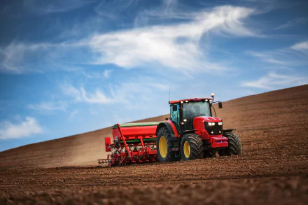 A bright blue sky stretches over a vast field, where a red tractor is plowing the earth, creating a striking scene in this HD desktop wallpaper.