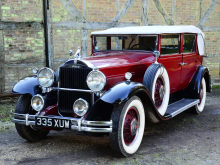 HD desktop wallpaper of a vintage car: maroon and black 1931 Packard Standard Eight Convertible Sedan vehicle with whitewall tires parked before a weathered brick wall.
