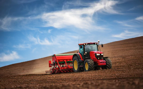 A bright blue sky stretches over a vast field, where a red tractor is plowing the earth, creating a striking scene in this HD desktop wallpaper.