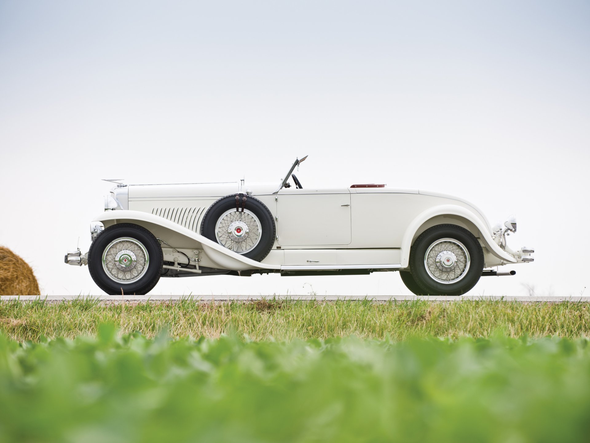 Side view of a white 1929 Duesenberg Model J Convertible Coupe vintage car against a clear sky, featured as an HD PC desktop wallpaper background.