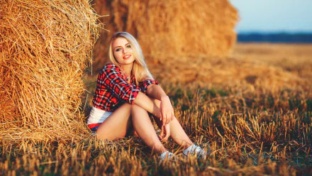 A blonde woman in a plaid shirt and denim shorts sits against a haystack in a field, smiling at the camera. HD desktop wallpaper and background.