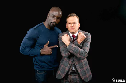 HD desktop wallpaper featuring two men in confident poses, with the one on the left pointing at himself and the one on the right crossing his arms.