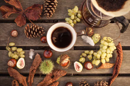 A fall-themed still life HD desktop wallpaper featuring a cup of coffee, grapes, autumn leaves, pinecones, and chestnuts arranged on a rustic wooden surface.