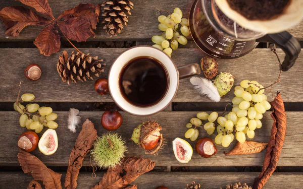 A fall-themed still life HD desktop wallpaper featuring a cup of coffee, grapes, autumn leaves, pinecones, and chestnuts arranged on a rustic wooden surface.