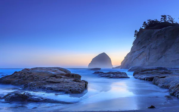 4K Ultra HD desktop wallpaper featuring a serene ocean coastline at horizon dusk, with rocky shores and natural cliffs under a clear blue sky.