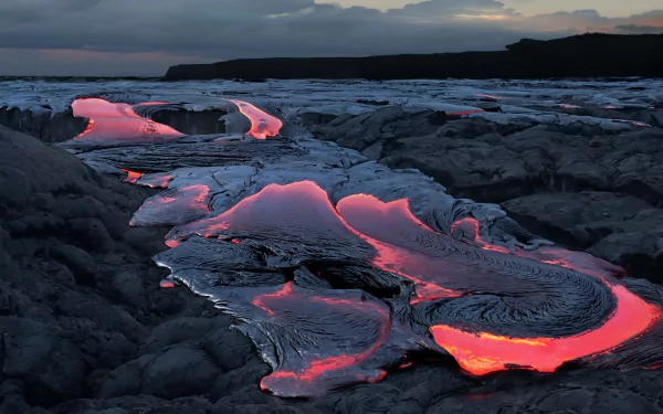 HD PC desktop wallpaper showing glowing lava flowing through dark volcanic rock under a cloudy sky, capturing the raw power of nature and an active volcano.