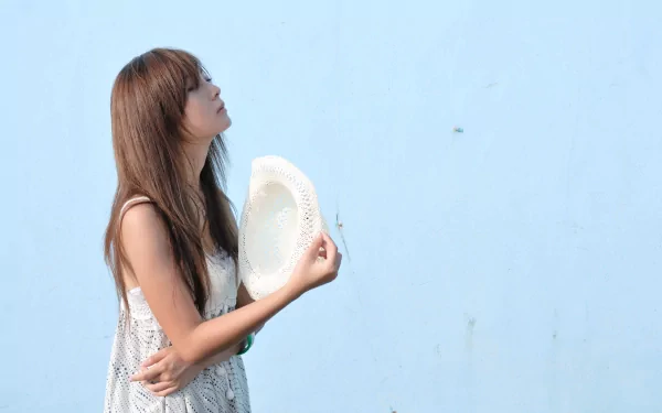 HD desktop wallpaper and background featuring Mikako Zhang Kaijie, a woman with long hair holding a hat against a light blue wall.