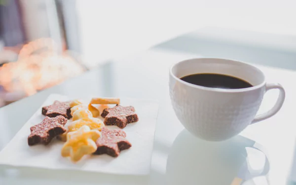A 4K Ultra HD desktop wallpaper featuring a white cup of coffee beside star and twist-shaped biscuits on a white surface.