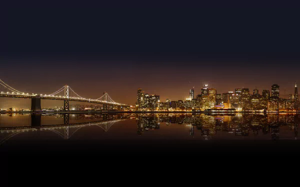 Nighttime 4K Ultra HD view of San Francisco city skyline with illuminated Bay Bridge, skyscrapers, and their reflections on calm water.