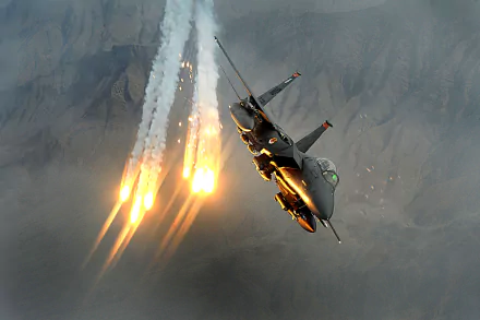A McDonnell Douglas F-15 Eagle jet fighter deploys flares mid-flight against a mountainous backdrop in this HD military warplane desktop wallpaper.