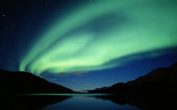 HD desktop wallpaper featuring the vibrant aurora borealis illuminating the night sky over a calm lake with silhouetted mountains in the background. Tag: nature.