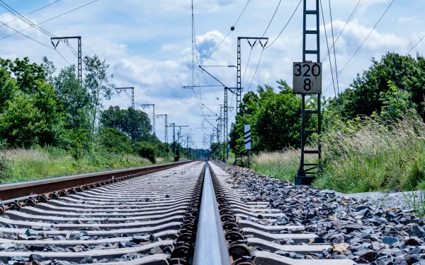 4K Ultra HD image of a man-made railroad stretching into the distance, surrounded by greenery under a partly cloudy sky, captured from ground level.