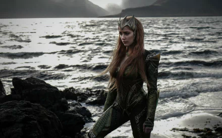 HD desktop wallpaper of Amber Heard as Mera from DC Comics’ Justice League. Mera is standing on a rocky shore with an ocean backdrop, wearing her iconic green suit and crown.