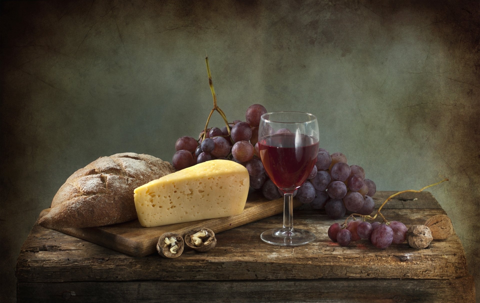 HD PC desktop wallpaper still life: crusty bread, wedge of cheese, walnuts, red wine in a glass and bunches of grapes on a rustic wooden board.