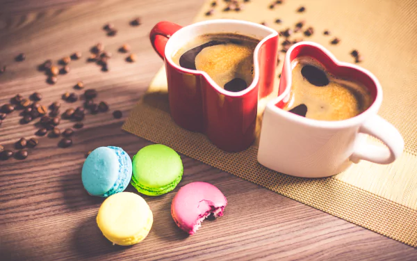 Heart-shaped coffee cups filled with coffee, surrounded by colorful macarons and scattered coffee beans on a wooden table, captured in 4K Ultra HD.