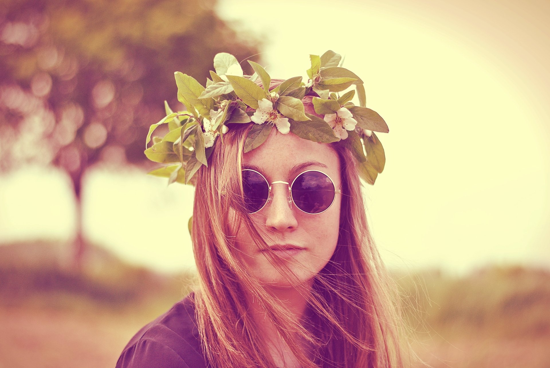 A woman model with a floral wreath on her head and round sunglasses, captured with a shallow depth of field in a soft, 4K Ultra HD desktop wallpaper.