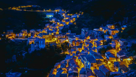 Night view of Castelmezzano, Italy, showing illuminated houses and town lights in a HD desktop wallpaper background.