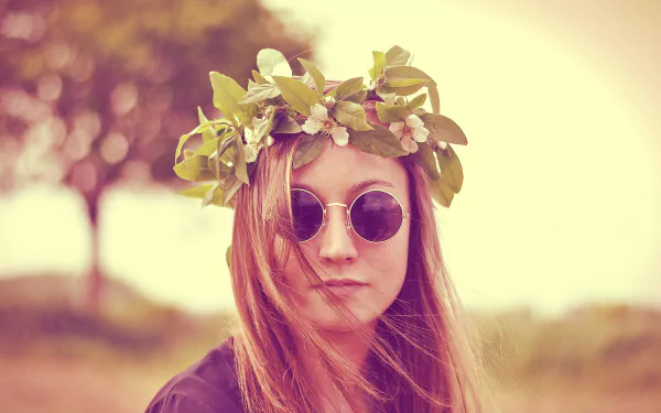 A woman model with a floral wreath on her head and round sunglasses, captured with a shallow depth of field in a soft, 4K Ultra HD desktop wallpaper.
