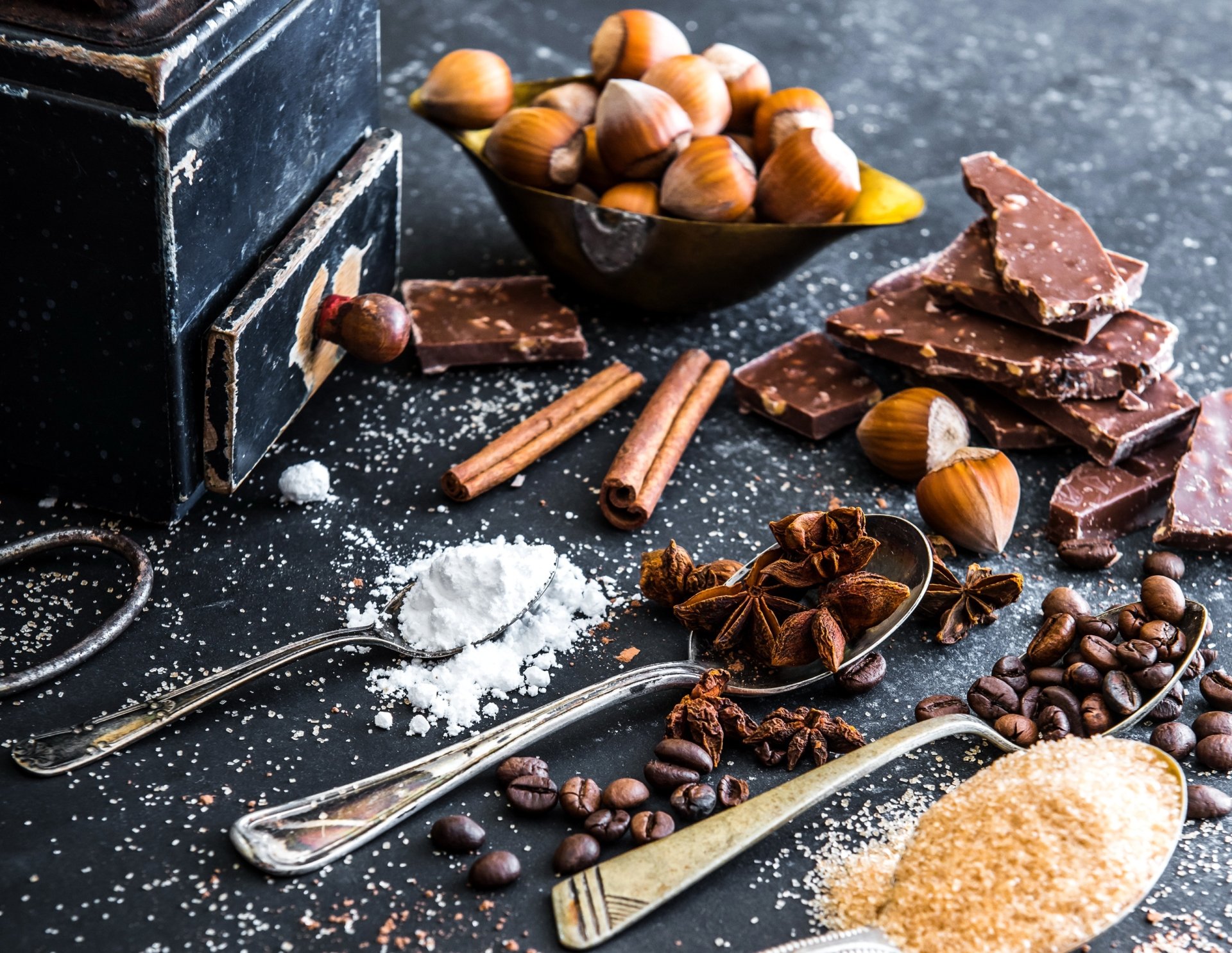 HD desktop wallpaper featuring a still life arrangement of sugar, star anise, coffee beans, chocolate, hazelnuts, and cinnamon sticks on a dark surface.