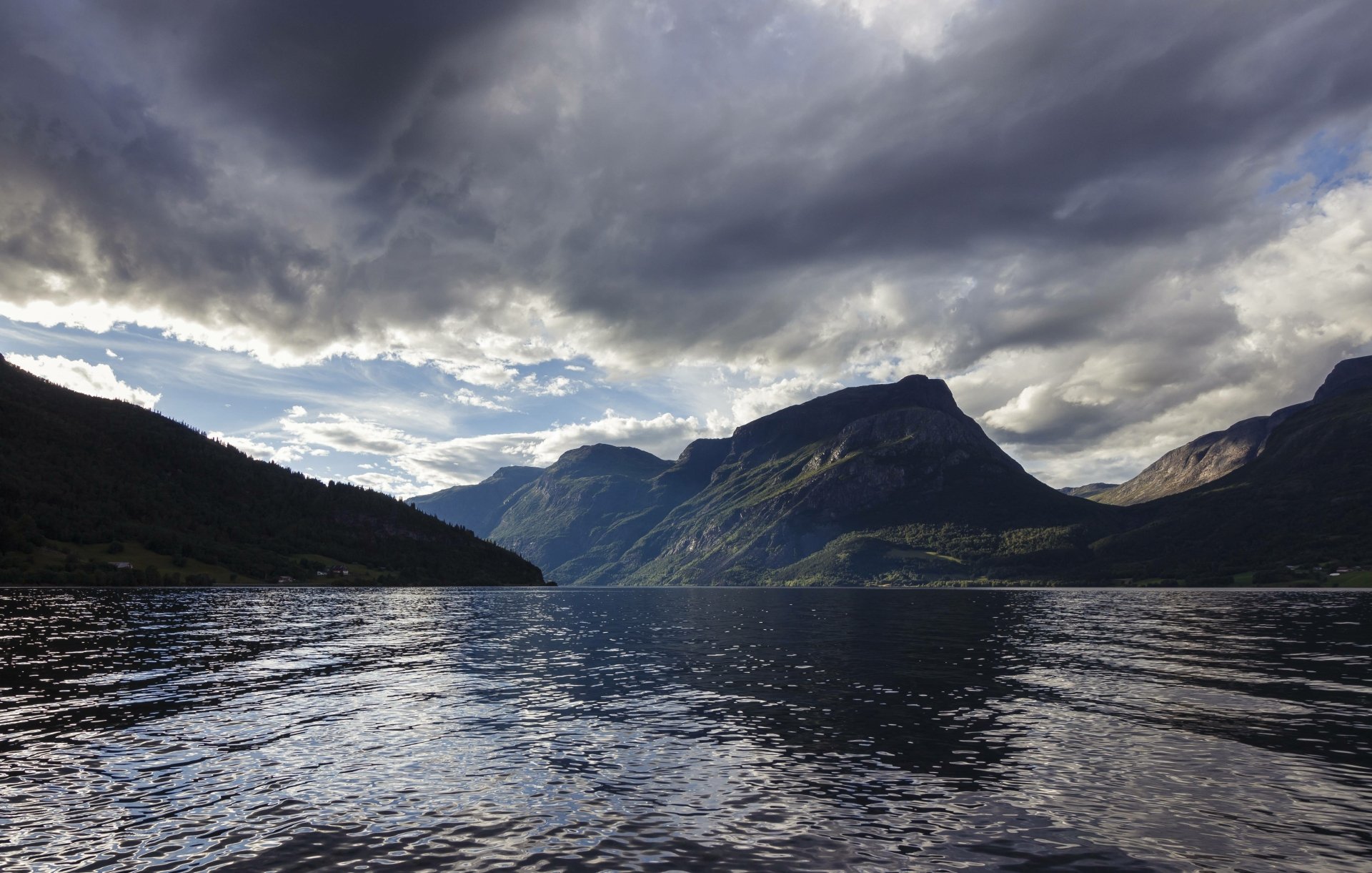 A serene view of Vangsmjøse lake in Norway, showcasing calm waters, dramatic mountains, and a cloudy sky. This stunning landscape makes for an inspiring HD desktop wallpaper.