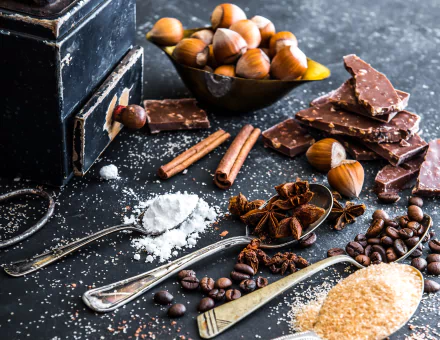 HD desktop wallpaper featuring a still life arrangement of sugar, star anise, coffee beans, chocolate, hazelnuts, and cinnamon sticks on a dark surface.