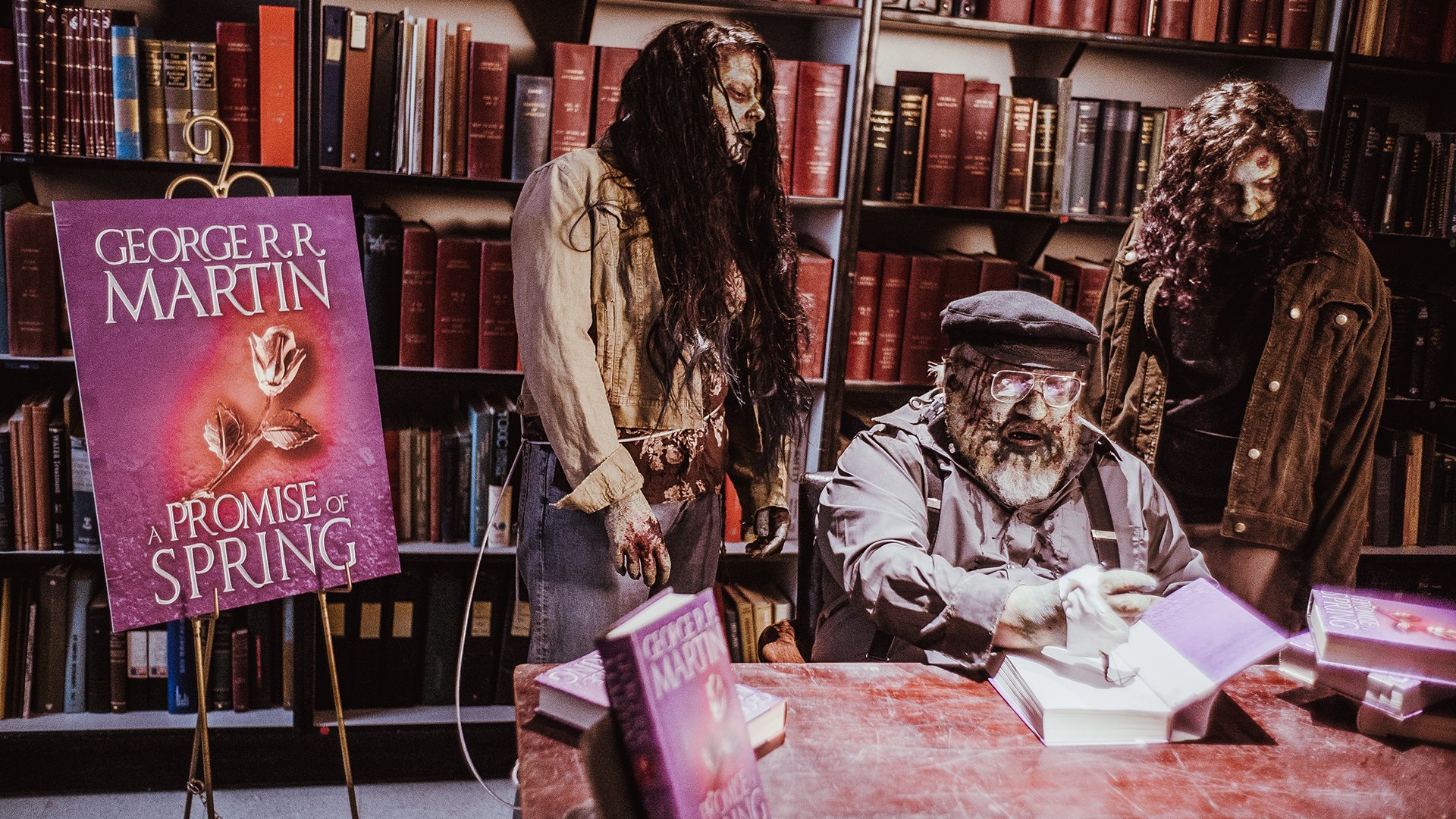 A zombie-themed HD desktop wallpaper from the TV show Z Nation, featuring zombie characters in a library setting, with a prominent book by George R.R. Martin in the foreground.