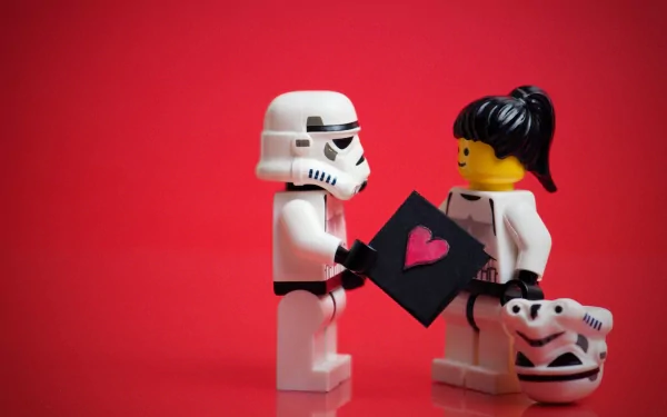 A creative HD desktop wallpaper featuring LEGO figures of a Stormtrooper offering a card with a heart to another LEGO figure holding a Stormtrooper helmet, set against a bright red background.