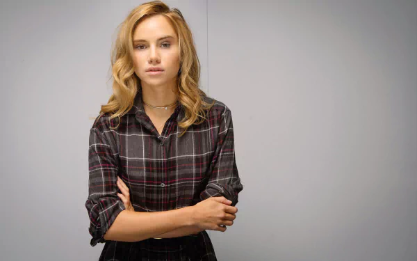 HD desktop wallpaper of a blonde woman with brown eyes in a plaid shirt, arms crossed and a neutral expression against a plain gray background.