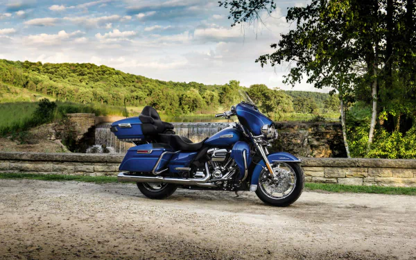 A blue Harley-Davidson Electra Glide Ultra Classic motorcycle parked on a scenic dirt path with greenery and a stone bridge in the background, shown as an HD desktop wallpaper.