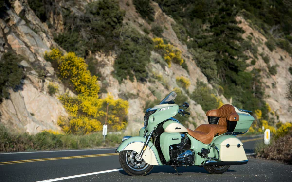 Indian Roadmaster motorcycle in mint green with tan leather seat parked on a mountain road with rocky cliffs and yellow flowers — HD PC desktop wallpaper/background