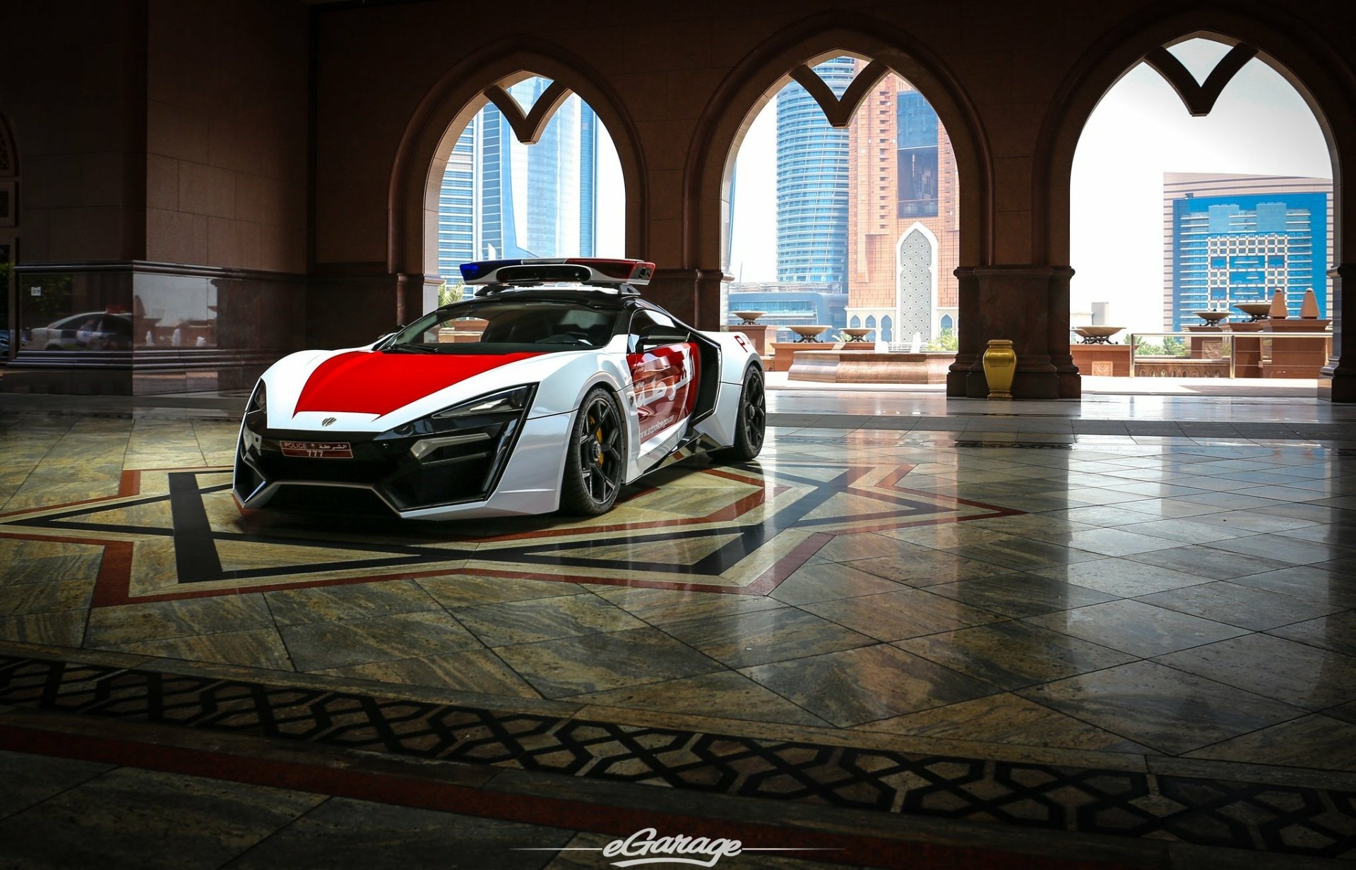 HD PC desktop wallpaper featuring a Lykan HyperSport parked inside an ornate building with city skyscrapers visible through arched windows.
