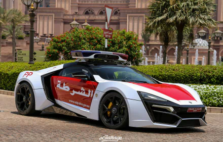 HD desktop wallpaper featuring a Dubai police car, the sleek Lykan HyperSport, parked in an urban setting with greenery and ornate buildings in the background.