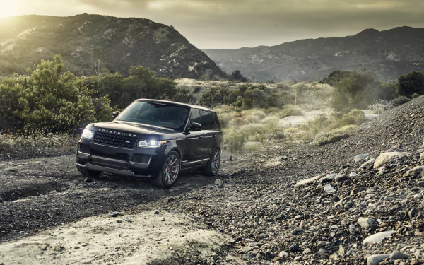 Black Land Rover Range Rover SUV parked on a rugged trail with mountains and greenery in the background, captured in 4K Ultra HD.