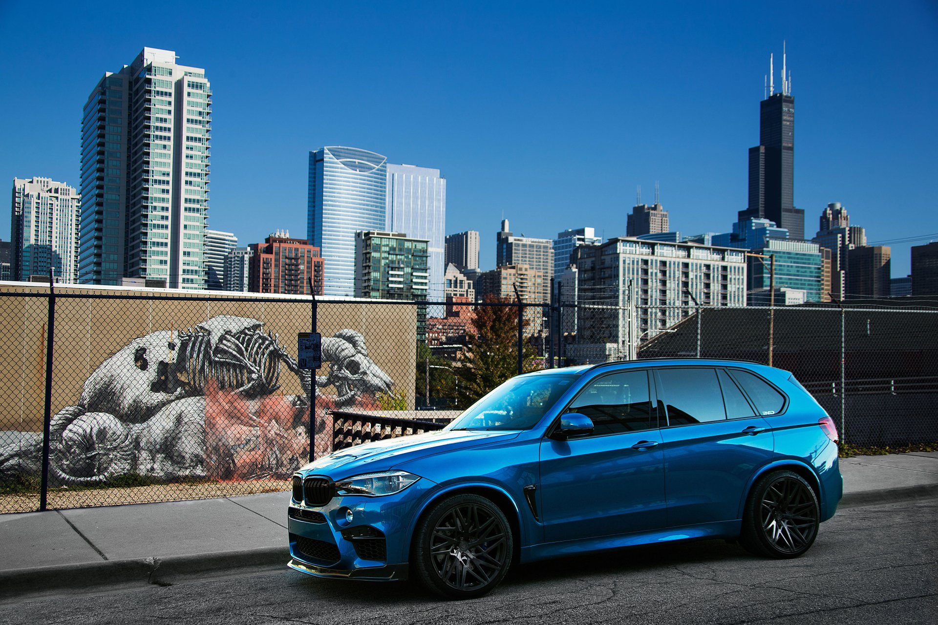 A blue BMW X5 SUV parked in front of an urban skyline with skyscrapers and street art, captured in a 4K Ultra HD desktop wallpaper.