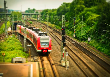 Tilt-shift effect showcases a red train traveling on railroad tracks surrounded by green foliage in this sharp 4K Ultra HD desktop wallpaper and background.