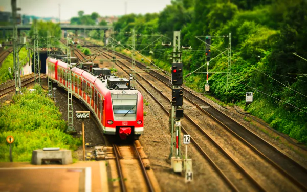 Tilt-shift effect showcases a red train traveling on railroad tracks surrounded by green foliage in this sharp 4K Ultra HD desktop wallpaper and background.