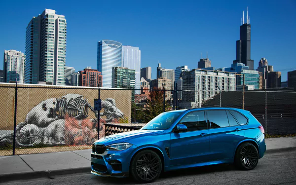 A blue BMW X5 SUV parked in front of an urban skyline with skyscrapers and street art, captured in a 4K Ultra HD desktop wallpaper.